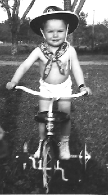 Photo of Doc C at 22 months riding a bicycle with a cowboy hat and bandana